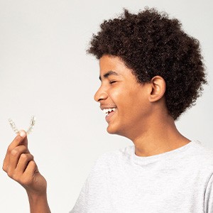 Profile view of teen in gray t-shirt smiling and holding Invisalign