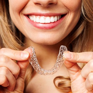 Woman smiling while holding Invisalign clear aligner