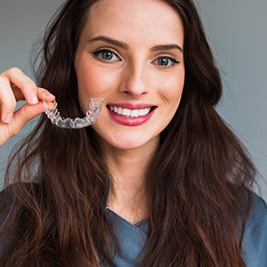 A young woman holding an Invisalign aligner next to her face