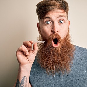 A surprised man holding a damaged Invisalign aligner