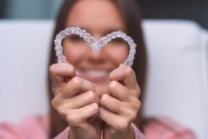 Woman holding two Invisalign trays in the shape of a heart with her face blurry in the background